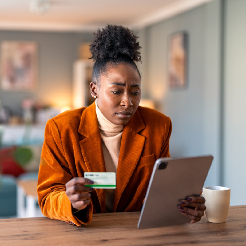 concerned woman holding credit card while viewing tablet screen