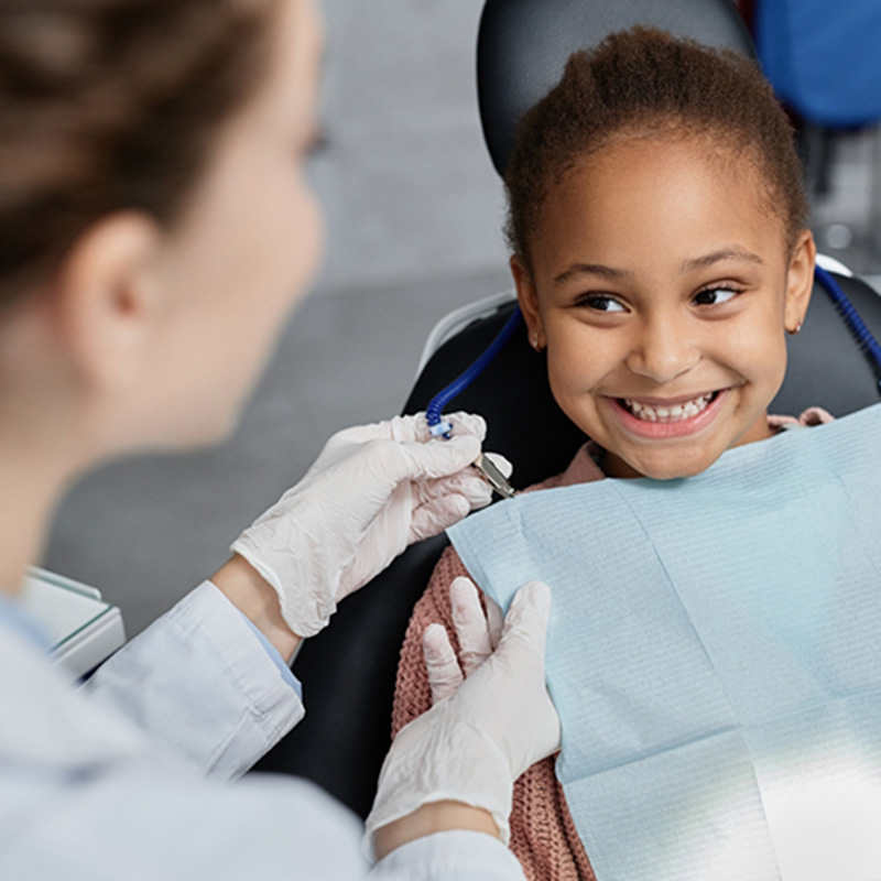 Over-the-shoulder view of dental hygienist. Shows young child smiling in the dentist's chair.